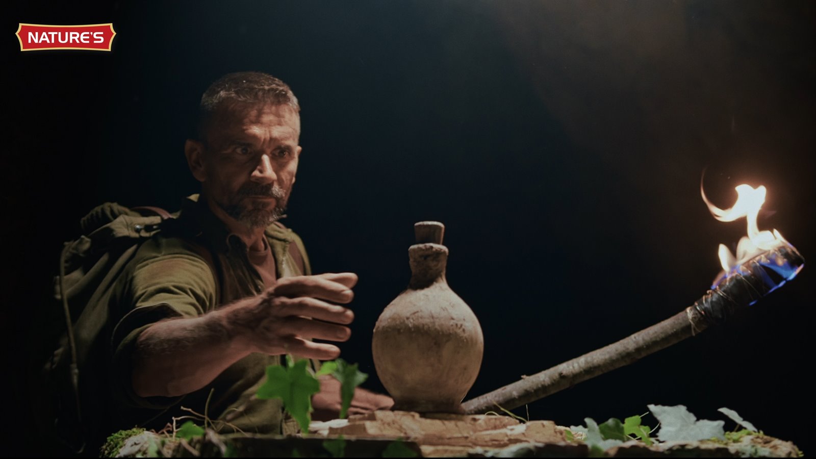 Man reaching for a clay flask beside a burning torch